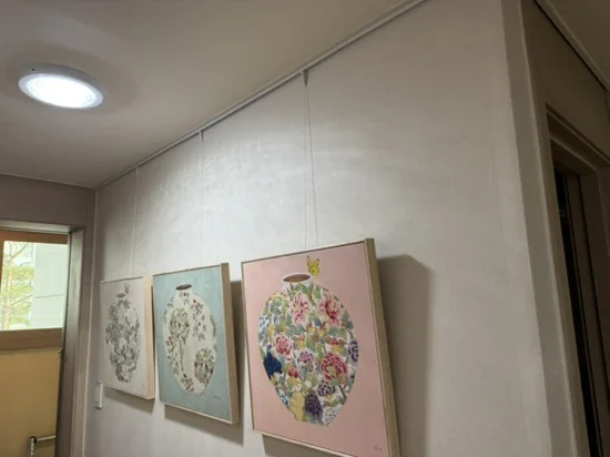 천장 쪽 노출형 액자레일에 액자 세 점을 나란히 건 현관 벽