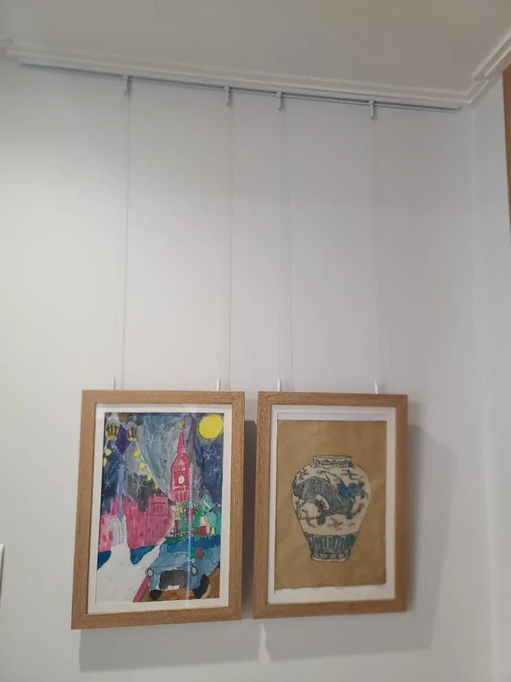 문 사이 1m 벽의 액자레일에 아이 그림 두 점을 낮게 건 모습